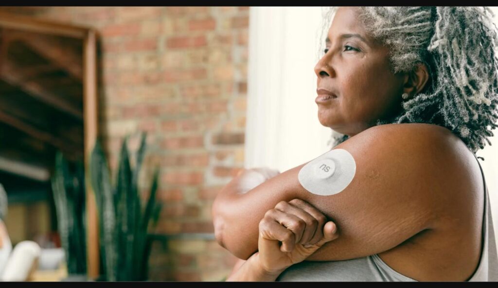 Mature woman wearing a continuous glucose monitor sensor patch on her upper arm