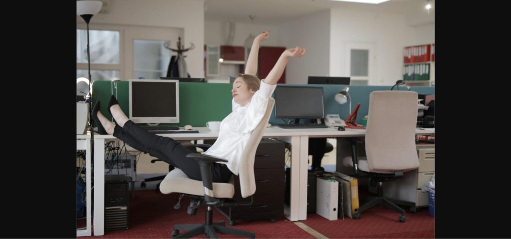 Woman happily stretching with arms raised at her office desk during a work break