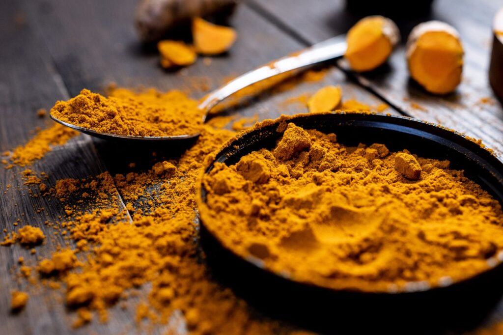 Close-up of vibrant turmeric powder with root on a rustic wooden table