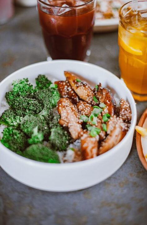 Meal prep chicken and rice bowl with broccoli, sesame seeds, and green onion in a white bowl