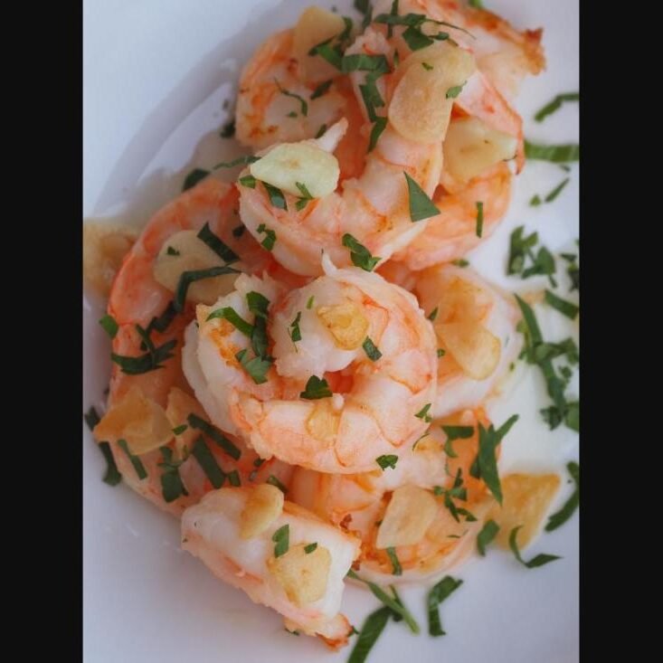 Garlic butter shrimp garnished with parsley on a white plate