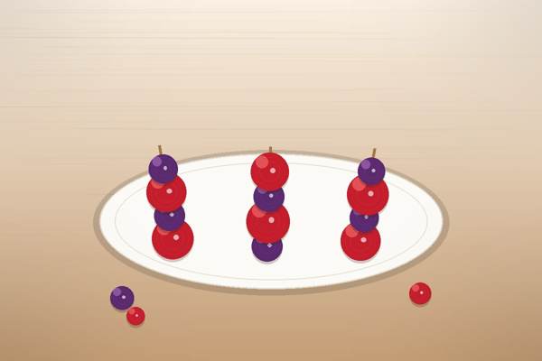 Three candied fruit skewers with glossy red strawberries and purple grapes coated in a crackly tanghulu sugar shell, arranged on a white plate on a rustic wooden table