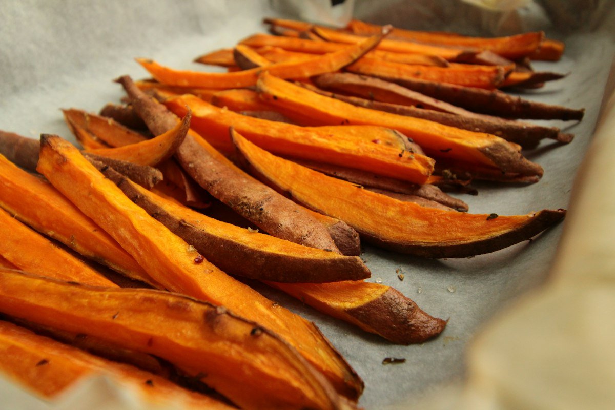 Golden sweet potato fries cut into even sticks on parchment paper