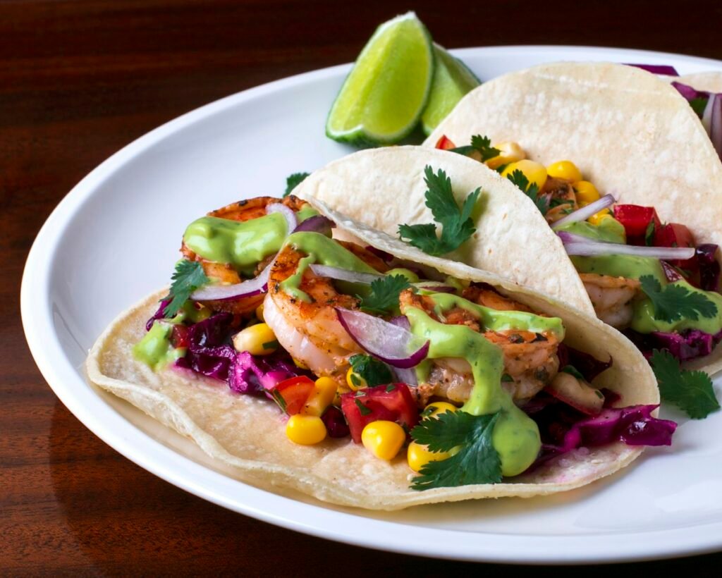 Easy shrimp tacos with purple cabbage slaw, corn and creamy lime sauce on a white plate