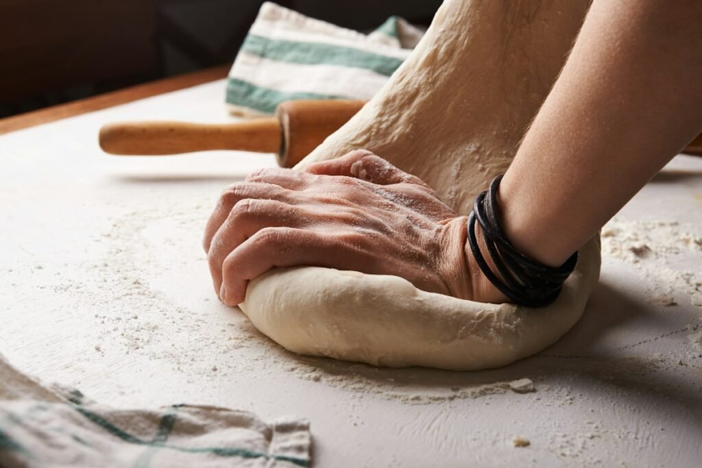 Hands kneading homemade pasta dough on a floured surface