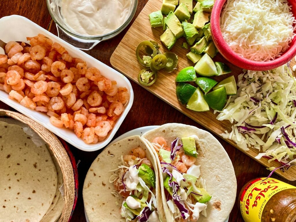 Shrimp taco ingredients: seasoned shrimp, warm tortillas, cabbage slaw, avocado and lime
