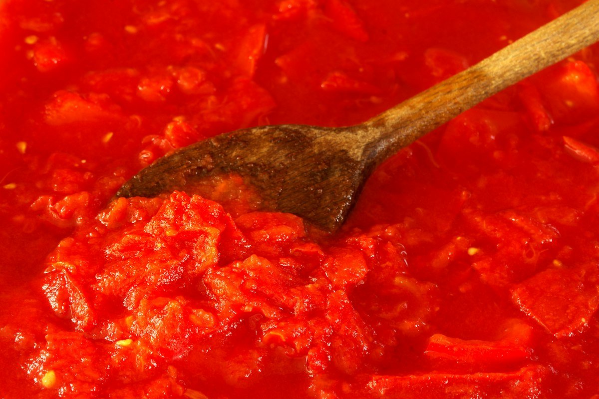 Tomato sauce being stirred with a wooden spoon